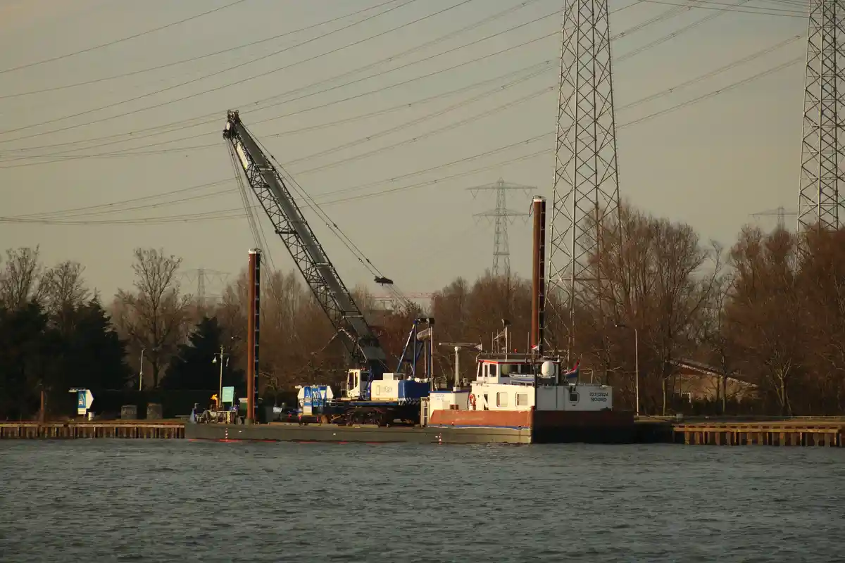 A barge with a large crane is docked on a river, surrounded by power lines and bare trees. The overlaid text reads 'i'm not…