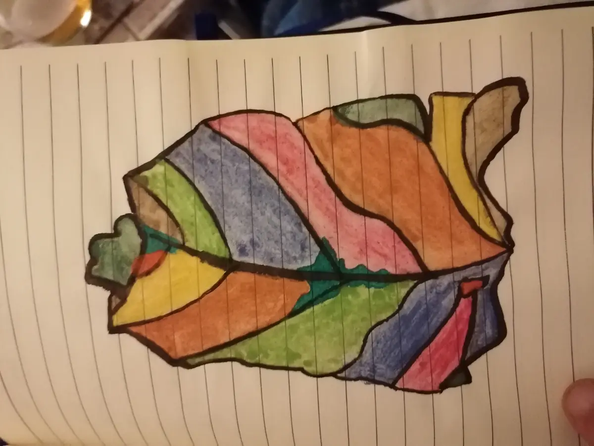 A child's crayon drawing on lined notebook paper depicts a colorful, abstract shape resembling a sandwich with various…