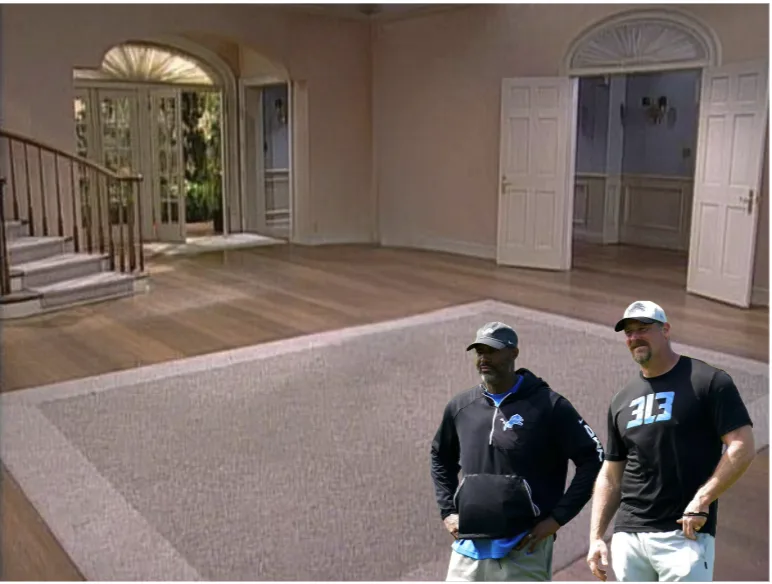 Two men stand in a large, empty, luxurious house with hardwood floors and arched doorways. One man wears a Detroit Lions…
