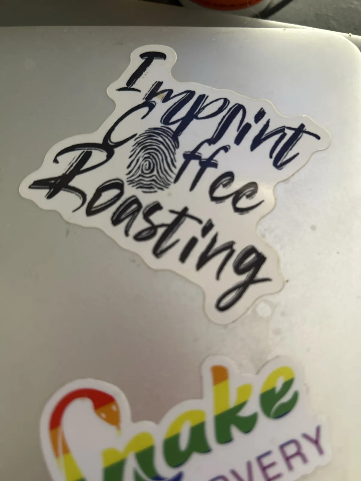 A close-up photo shows a white sticker with the words 'Imprint Coffee Roasting' in black cursive script, where the 'o' in…