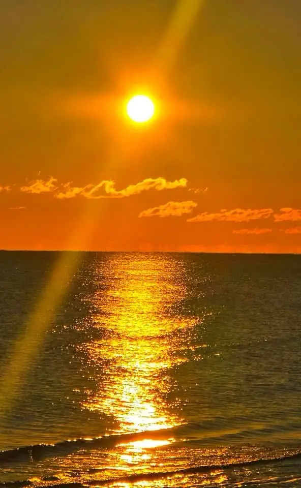 A vibrant sunset over the ocean with the sun low in the sky, casting golden light and reflections across the water. The sky…