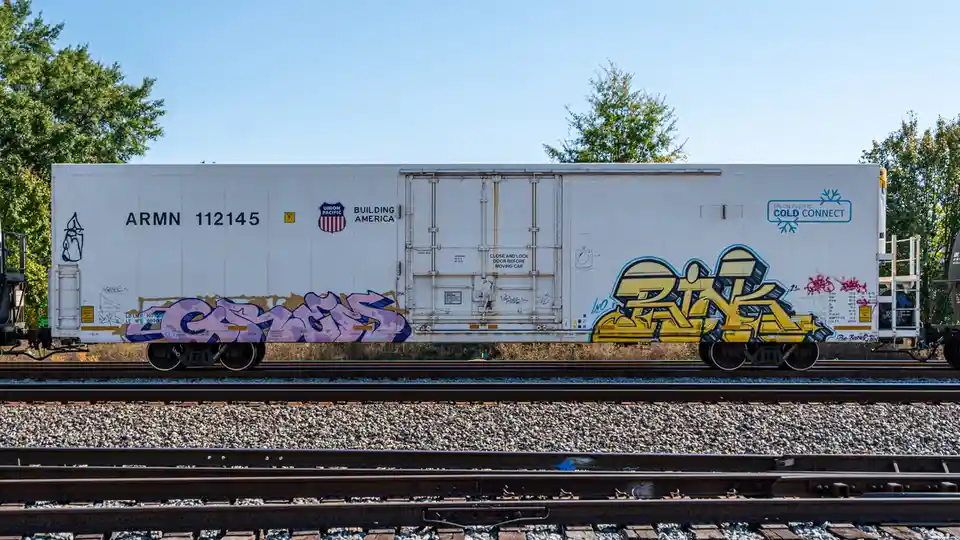 A white Union Pacific refrigerated railcar, marked 'ARMN 112145' and 'COLD CONNECT', sits on tracks with trees in the…