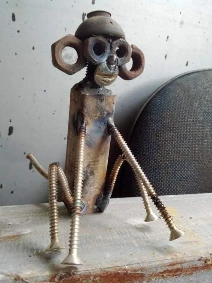 A handmade sculpture of a monkey crafted from metal parts including bolts, nuts, and a threaded rod for limbs, sitting on a…