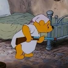a cartoon bear wearing a white nurse's uniform and cap, holding a wooden rifle while standing beside a metal bed frame in a…