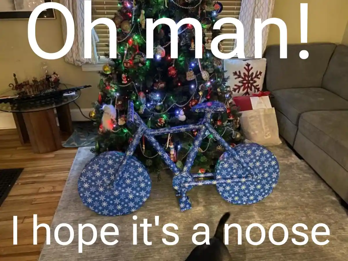 A decorated christmas tree stands in a living room with a large bicycle-shaped object made of blue wrapping paper with white…