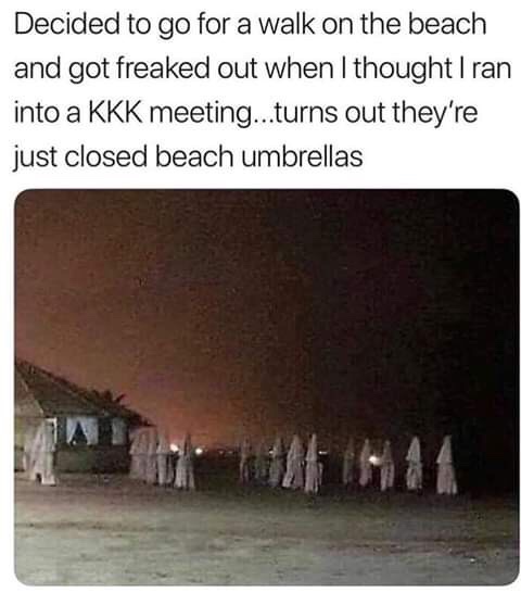 A nighttime beach scene shows a row of closed, white beach umbrellas standing upright in the sand, creating a silhouette…