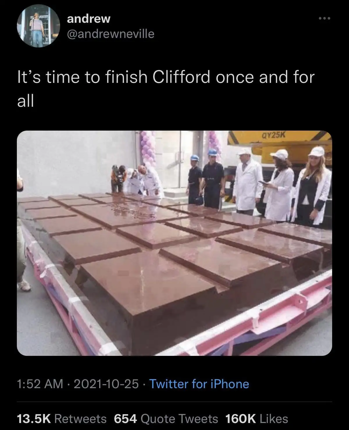 A large, oversized chocolate bar, segmented into squares, sits on a pink pallet. Several people in white lab coats and hard…