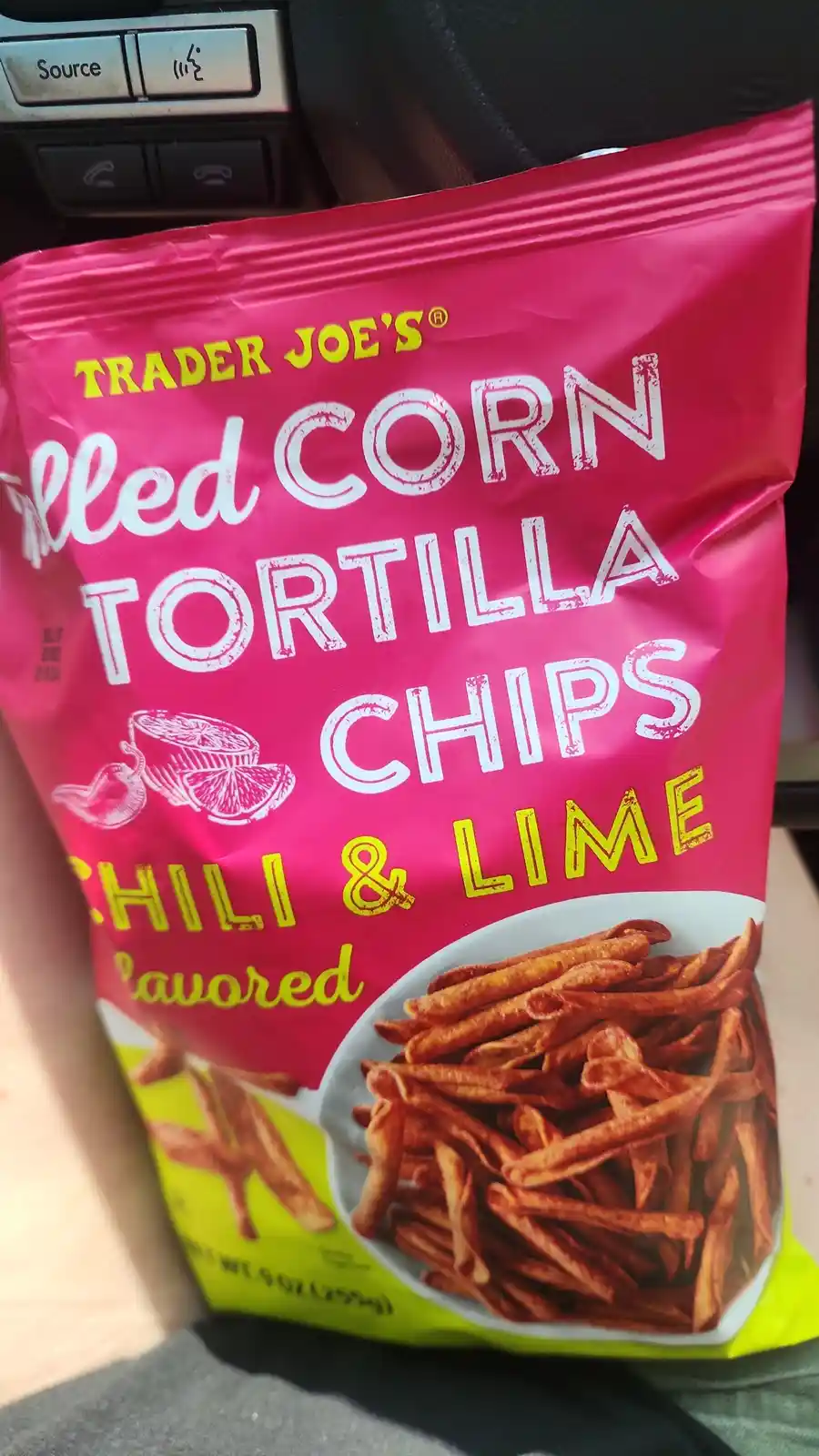 A close-up photo shows a pink and yellow bag of Trader Joe's 'Chili & Lime' flavored 'Filled Corn Tortilla Chips' resting on…