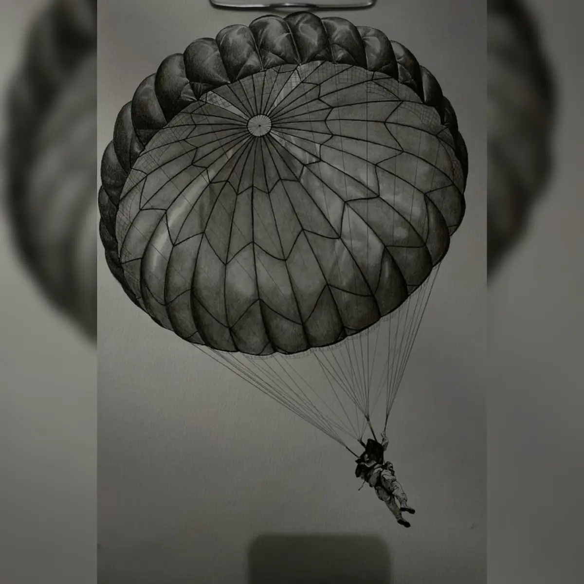 A detailed pencil drawing shows a parachutist descending with a fully deployed parachute against a plain background. The…
