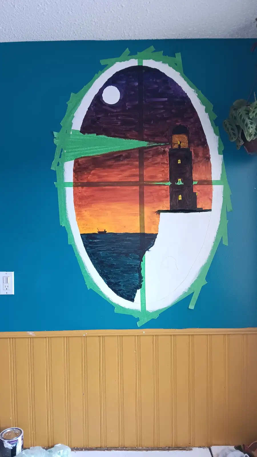 A wall mural in progress shows a large oval painted with a sunset scene featuring a lighthouse, but the top half is painted…
