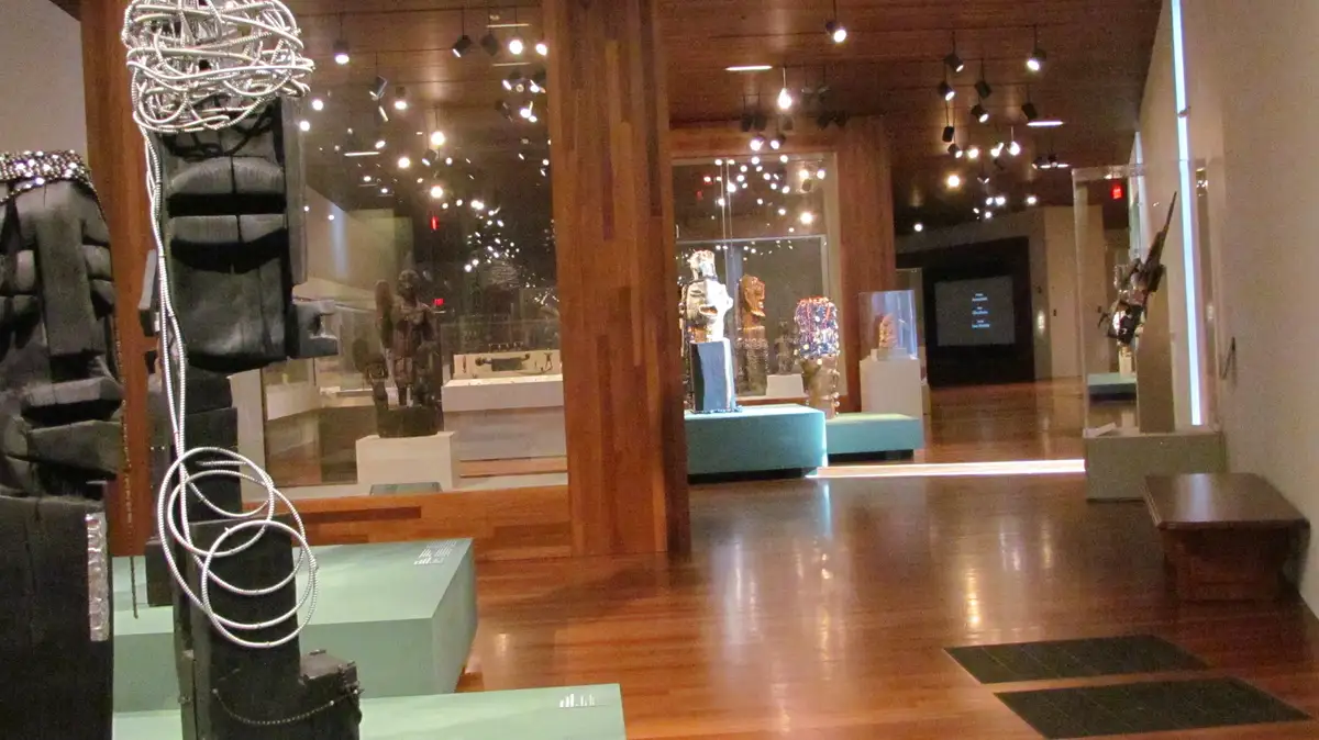 An interior shot of a museum gallery with wooden floors, glass display cases, and various sculptures and artifacts on…