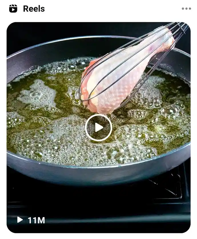 A raw chicken leg is visibly held by a metal whisk above a frying pan filled with hot, bubbling oil. The image is a still…
