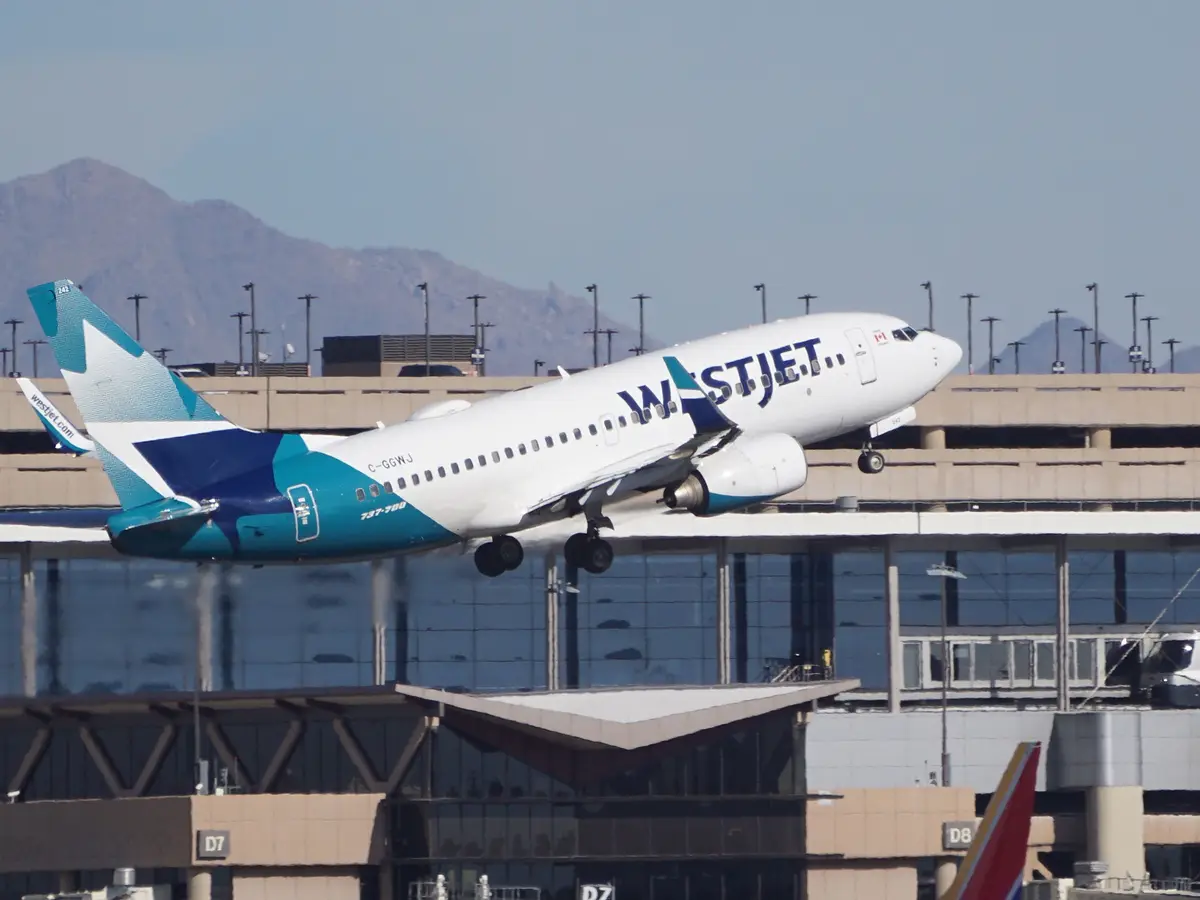 A WestJet Boeing 737-700 airplane, registration C-GGWJ, is captured mid-takeoff, its landing gear still down as it ascends…