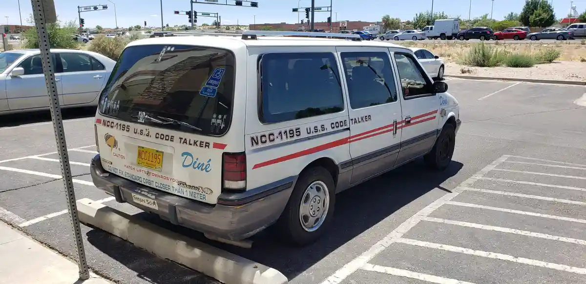 A white Dodge Caravan minivan parked in a lot, decorated with Star Trek-themed decals including 'NCC-1195 U.S. CODE TALKER'…