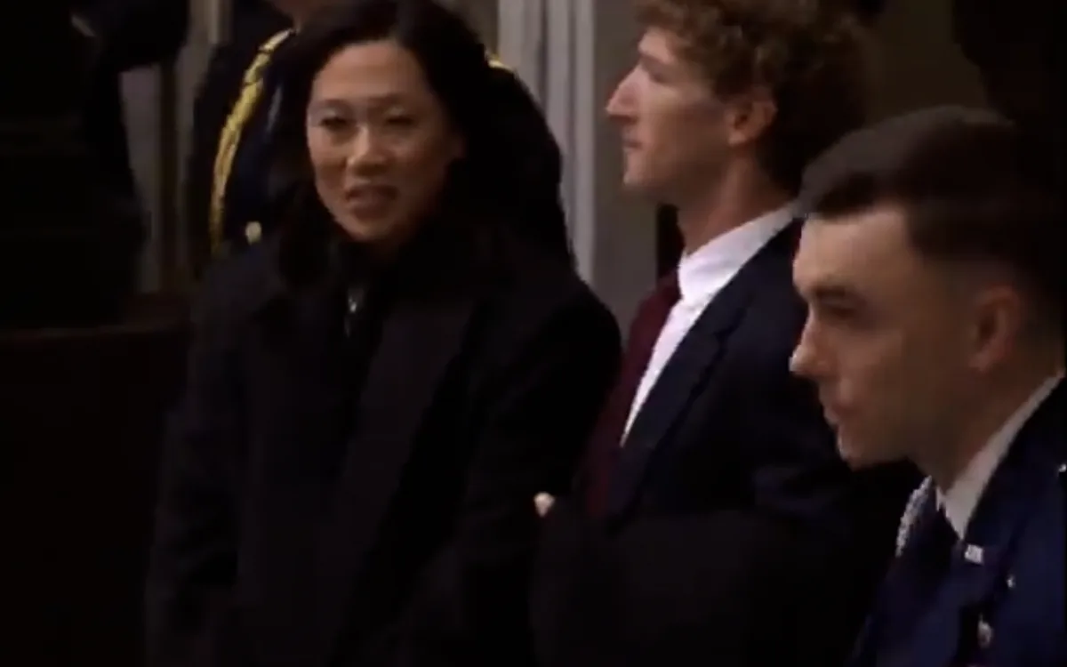A still image shows three people standing in a formal setting, likely a ceremony or official event. The woman in the center…
