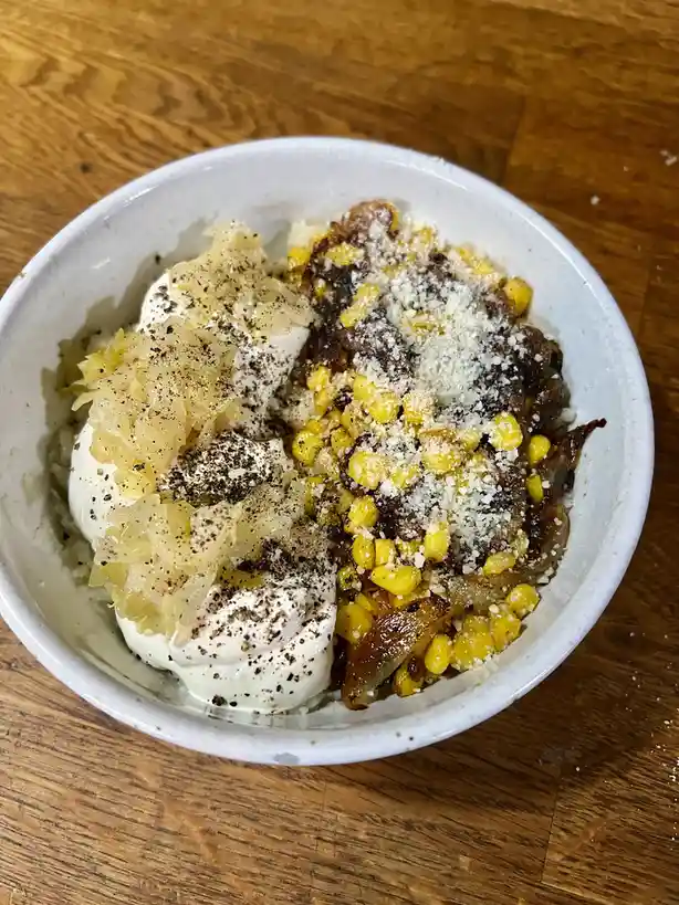 A white bowl on a wooden table contains two distinct halves of food: one side has creamy white yogurt topped with…