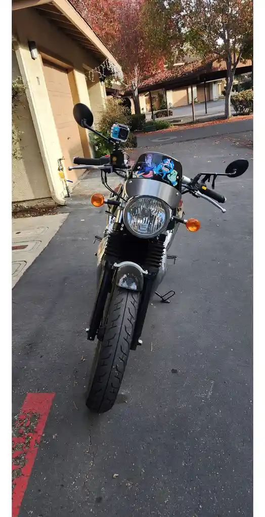 A motorcycle is parked in a residential driveway, facing the camera. A small action camera is mounted on the handlebars, and…