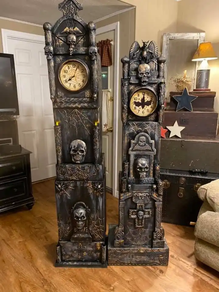 Two ornate, black, gothic-style grandfather clocks stand side-by-side in a living room, both heavily decorated with skulls…