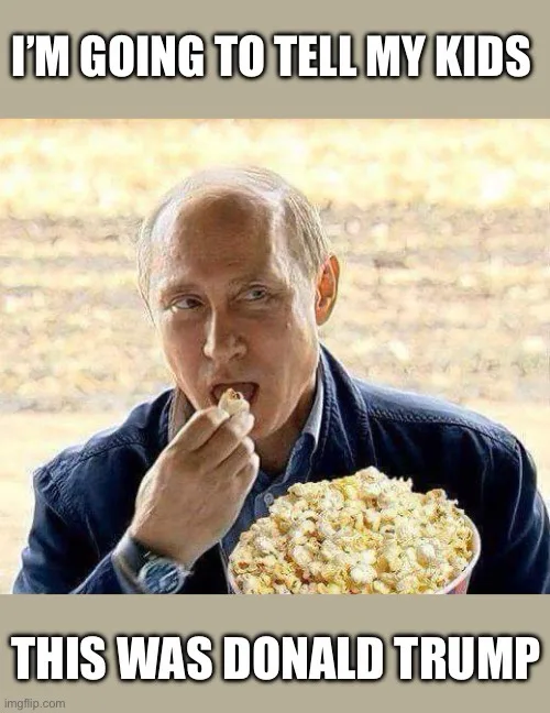 A man with receding hairline and a watch is eating popcorn while looking intently at the camera. He holds a large bowl of…