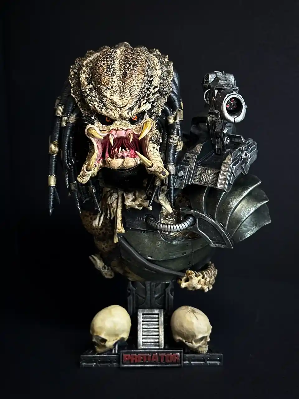 A highly detailed Predator action figure bust with a roaring, open-mouthed expression, wearing armor and carrying a…