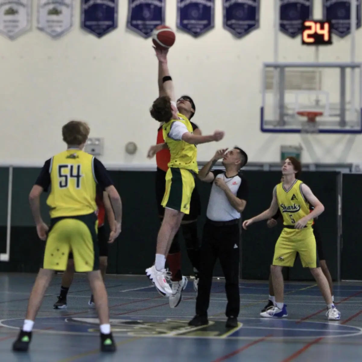 A basketball player in a yellow jersey leaps high to shoot the ball while being closely guarded by an opponent in a red…