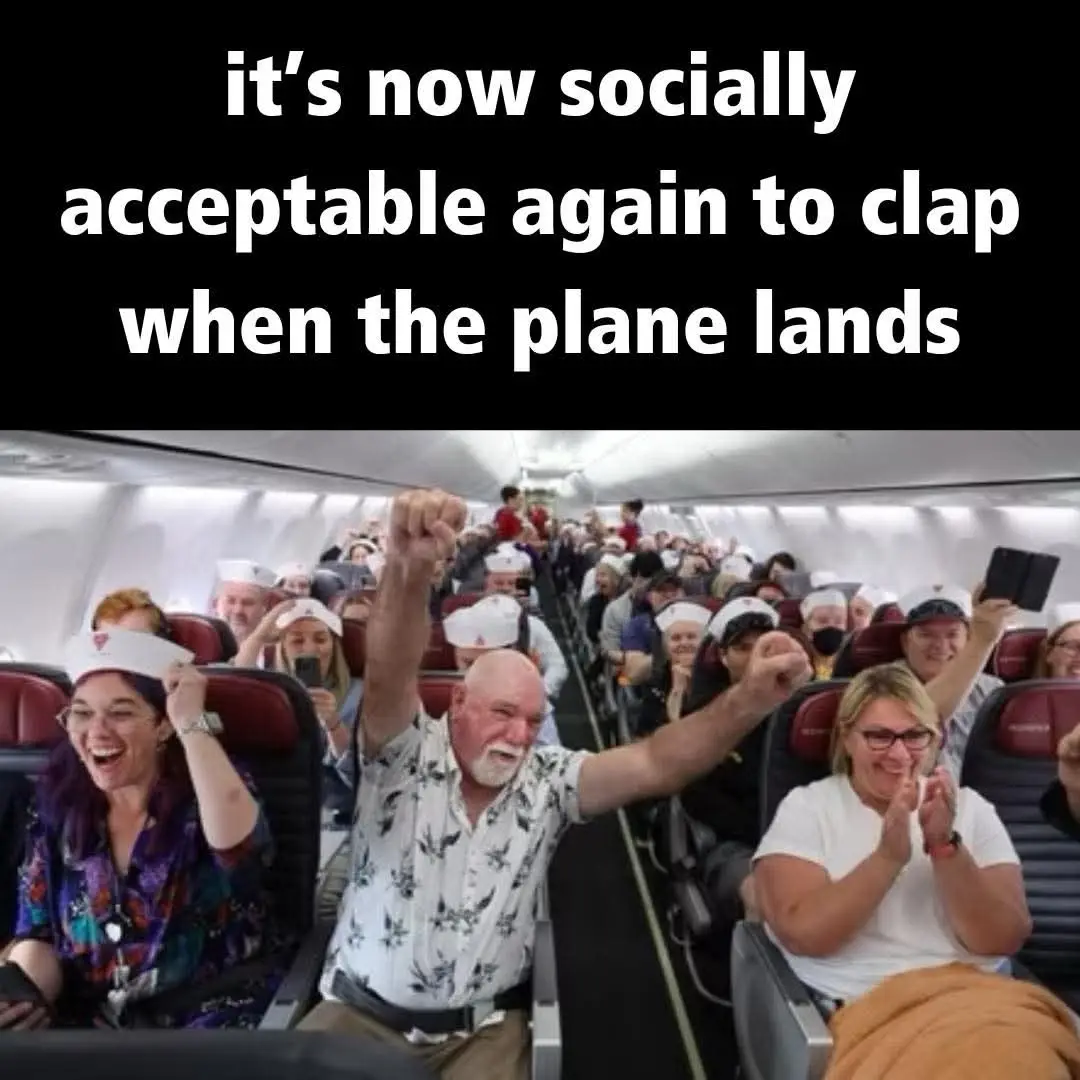 An airplane cabin filled with passengers, many wearing white hats, enthusiastically clapping and cheering as if celebrating…