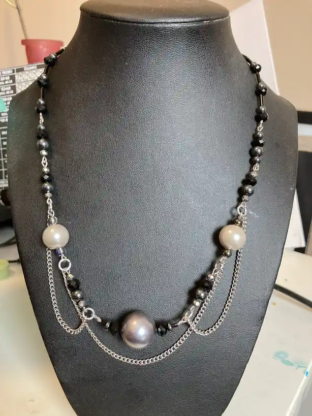 A handmade necklace with black and silver beads and pearls is displayed on a black mannequin bust. The text overlay reads 'i…