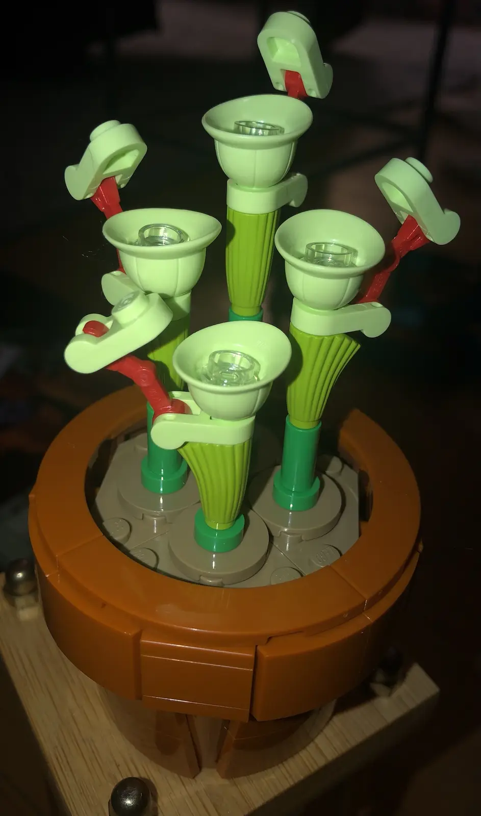 A close-up photo shows a Lego flower arrangement with multiple light-green, fluted stems and cup-shaped blossoms, each…