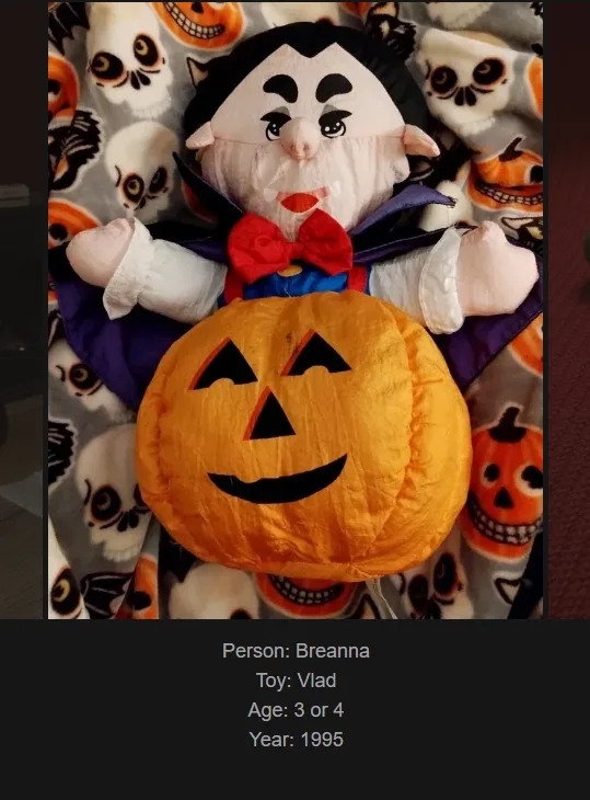 A plush toy resembling a vampire with black hair, white face, red bowtie, and purple cape, holding a large orange pumpkin…