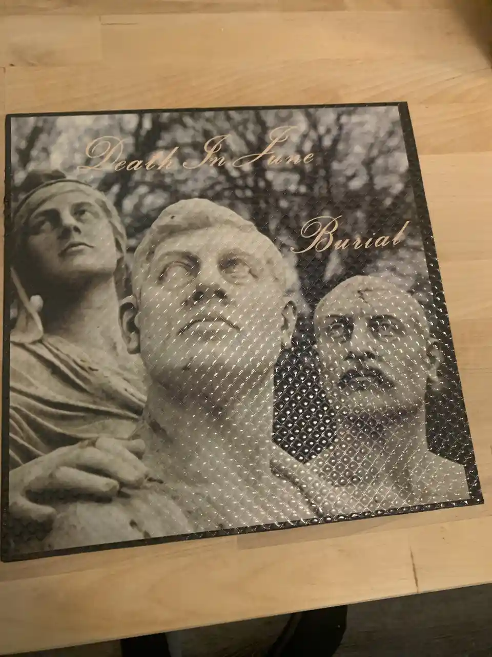 A black-and-white album cover for 'Death In June' titled 'Burial' featuring three stone statues of men looking upward…