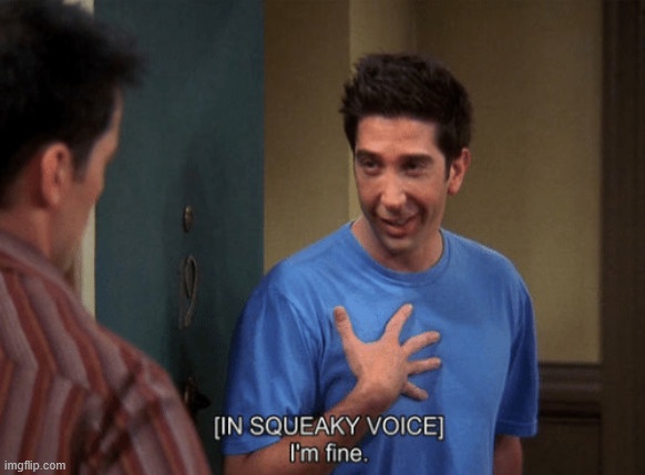 A man in a blue t-shirt places his hand over his heart while smiling and looking slightly embarrassed, as if feigning…
