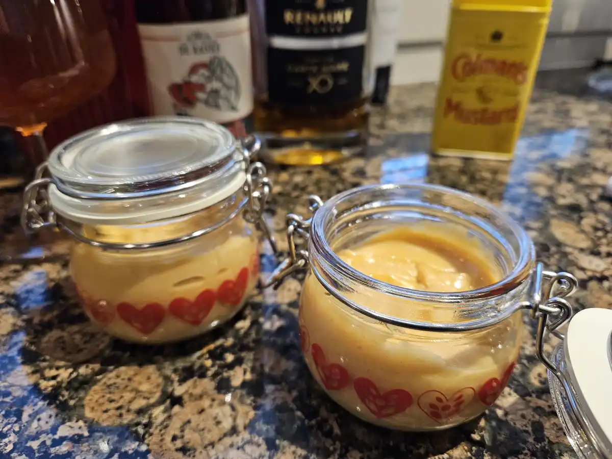 Two glass jars with metal clasp lids sit on a granite countertop, filled with a creamy yellow substance resembling homemade…