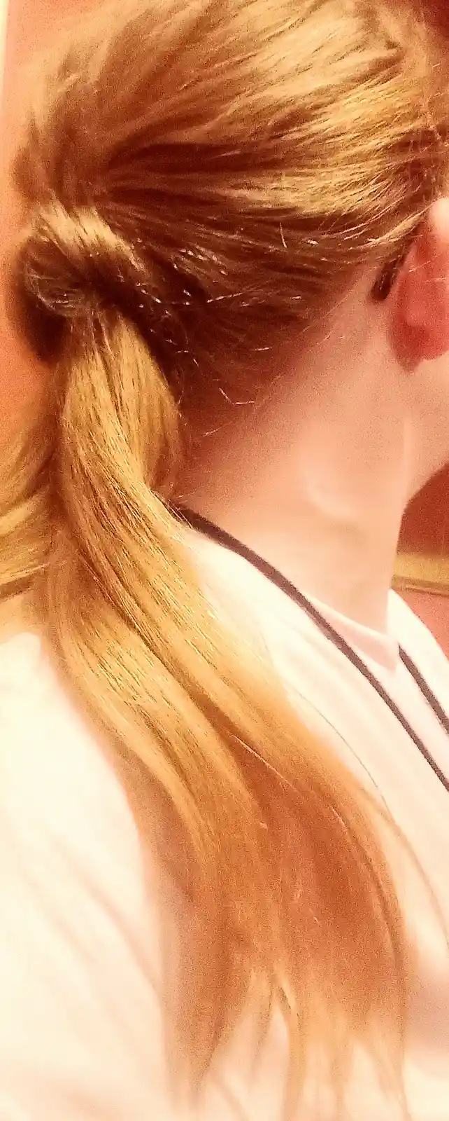 A close-up photo shows the back of a person with long, blonde hair styled in a low ponytail with a messy bun at the base…