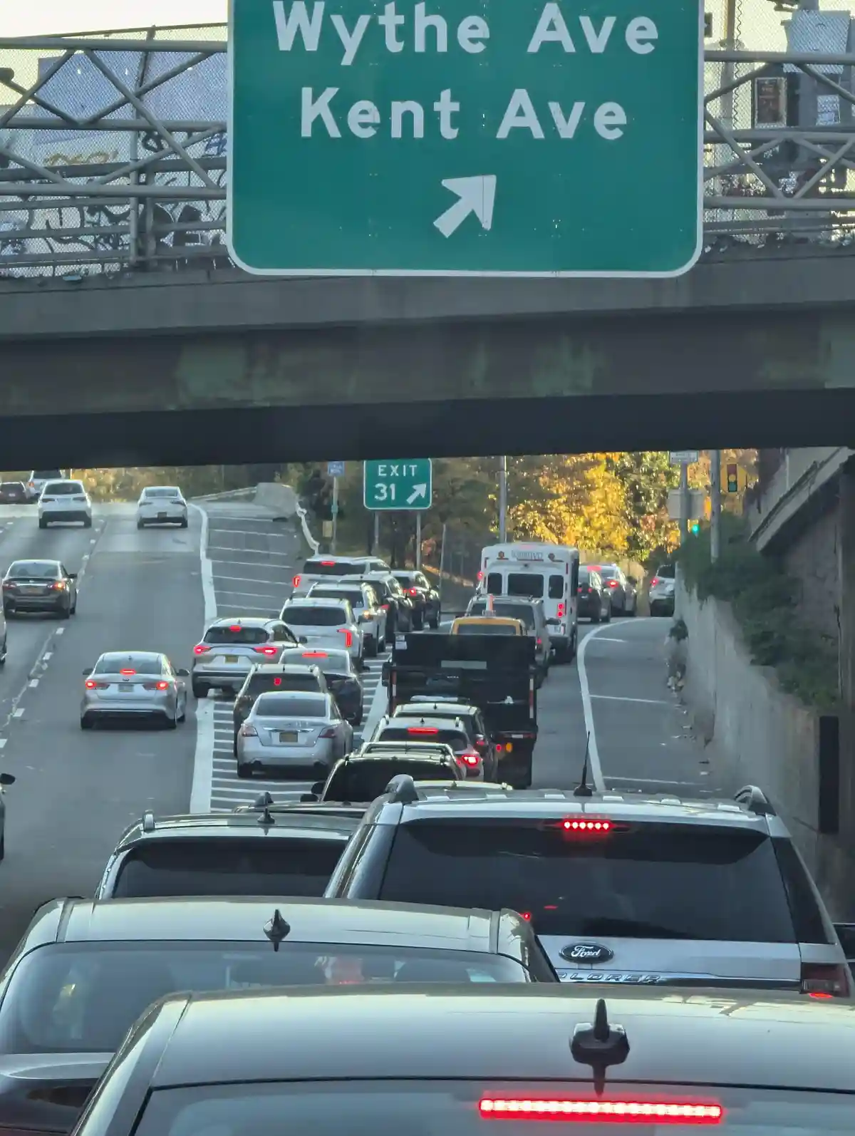 A photo taken from inside a car shows heavy traffic on a highway approaching an exit ramp. A large green overhead sign reads…