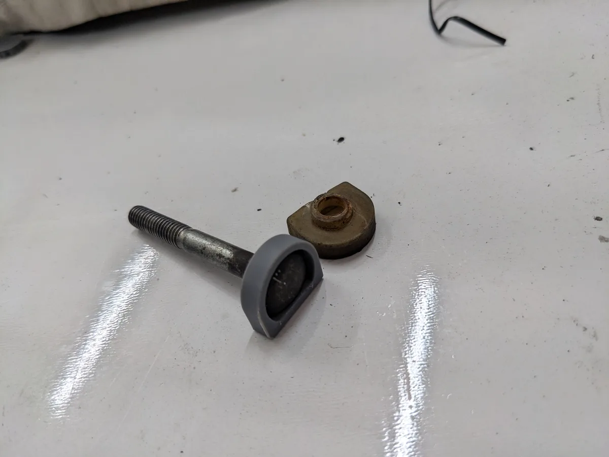 A close-up photo shows a metal bolt with a grey plastic cap and a square metal nut lying on a white, scratched surface. The…