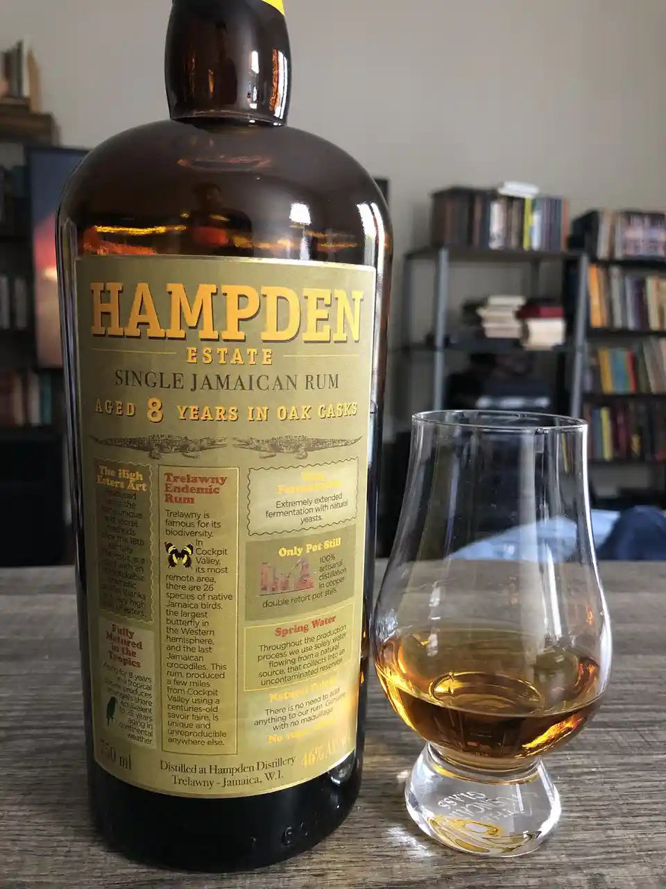 A bottle of Hampden Estate Single Jamaican Rum, aged 8 years, sits next to a tasting glass with a small amount of amber…