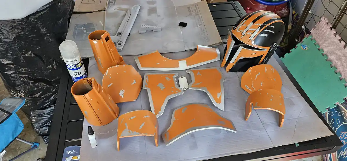A work-in-progress Mandalorian armor costume laid out on a table, with various orange-painted pieces showing white paint…