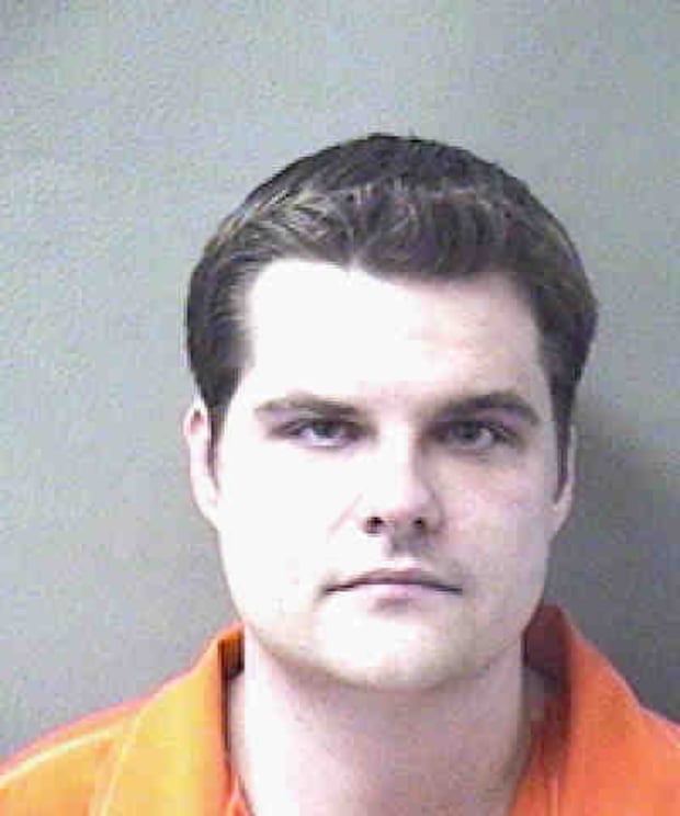 A mugshot of a man with dark hair wearing an orange jumpsuit against a plain gray background. The image has text overlaid at…