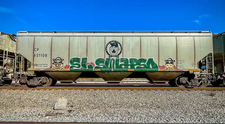 A silver Canadian Pacific freight train car, number CP 651108, is covered in graffiti. Large green stylized letters spell…