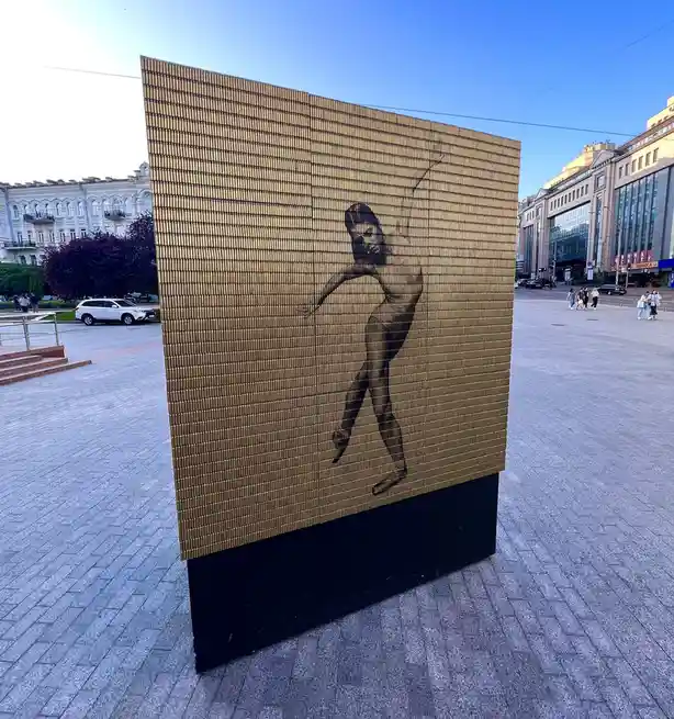 A large outdoor sculpture made of golden bullet casings arranged in a grid forms the silhouette of a woman dancing. The text…