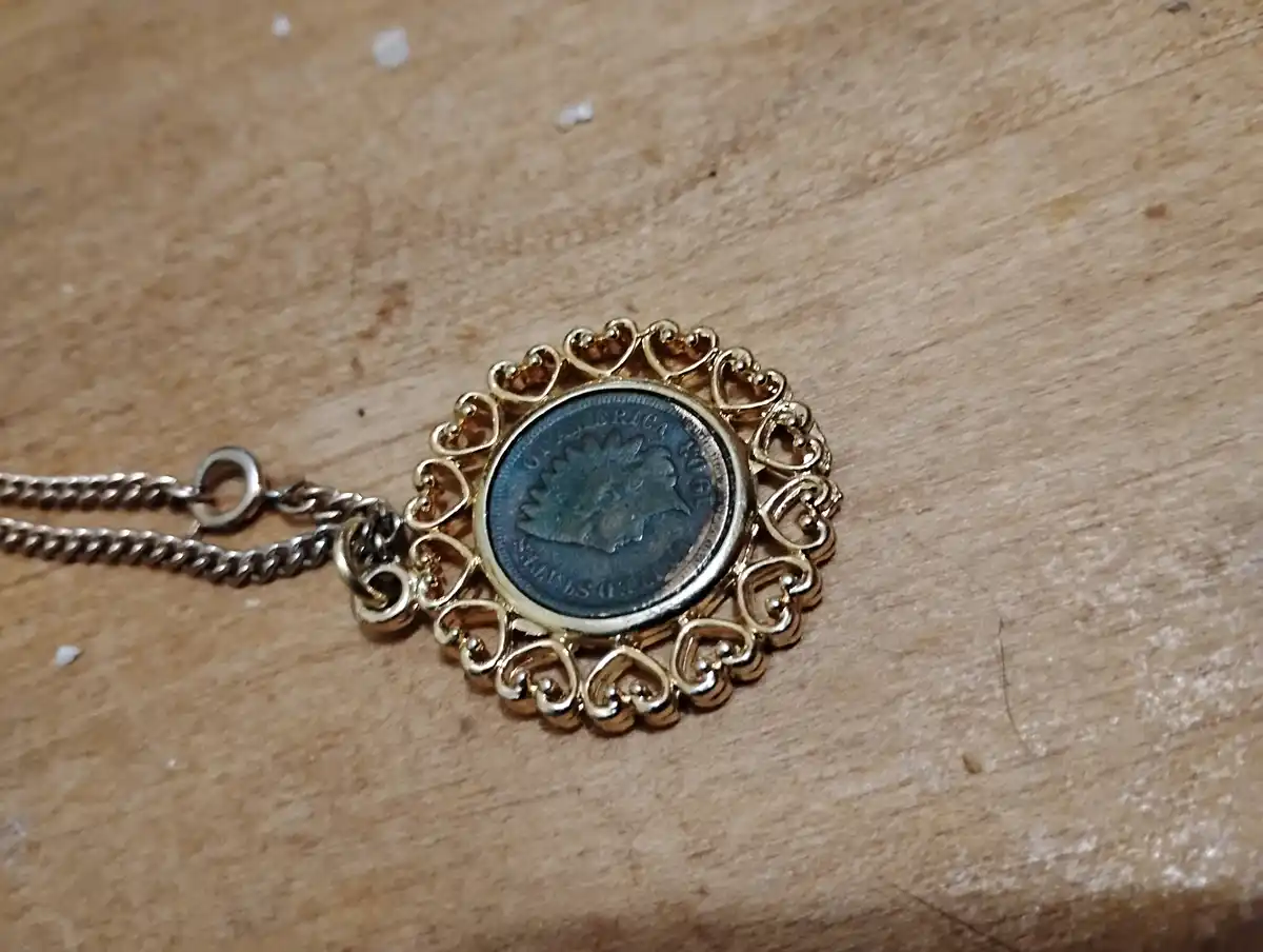 A close-up photo shows a necklace with a gold-colored pendant featuring a decorative heart-shaped border, holding a dark…