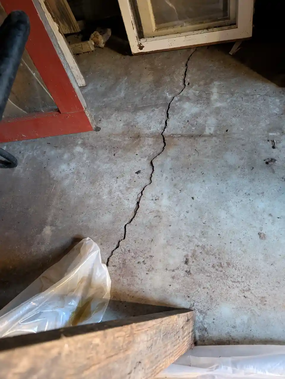 A close-up photo shows a large, jagged crack running diagonally across a weathered concrete floor inside what appears to be…