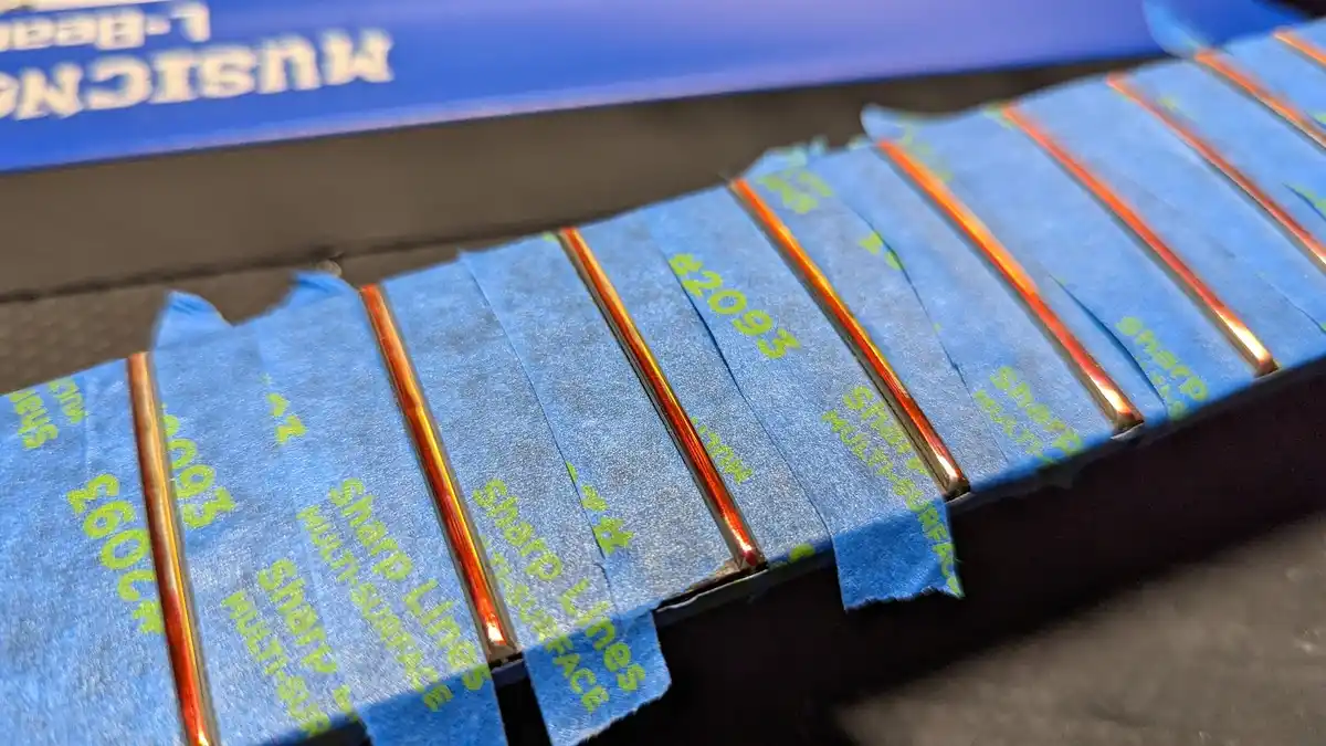A close-up photo shows multiple strips of blue painter's tape with green text reading 'sharp lines multi-surface' and…