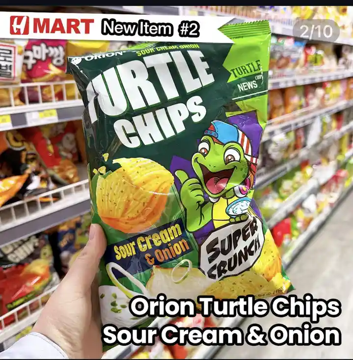 A hand holds a bag of Orion Turtle Chips in a H Mart grocery aisle, featuring a cartoon turtle mascot and 'Sour Cream &…