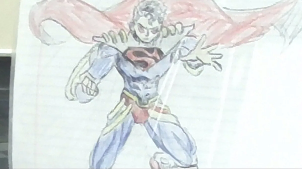 A child's crayon drawing of superman on lined paper, with a red cape and blue suit, overlaid with the text 'superman'. The…