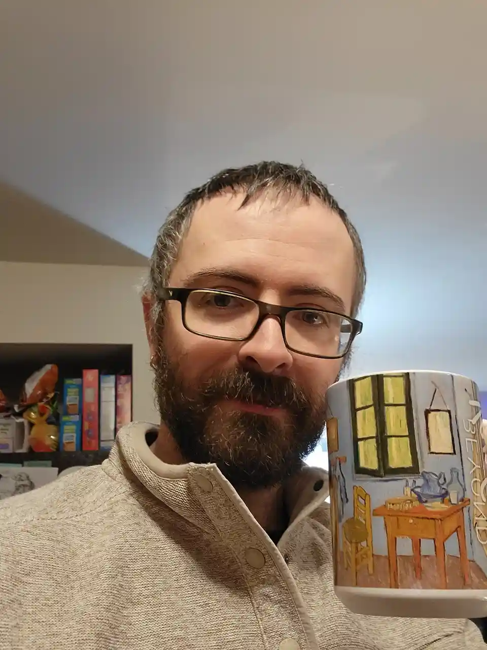 A man with glasses and a beard holds up a mug featuring Vincent van Gogh's 'The Bedroom' painting, with the word 'BEYOND'…