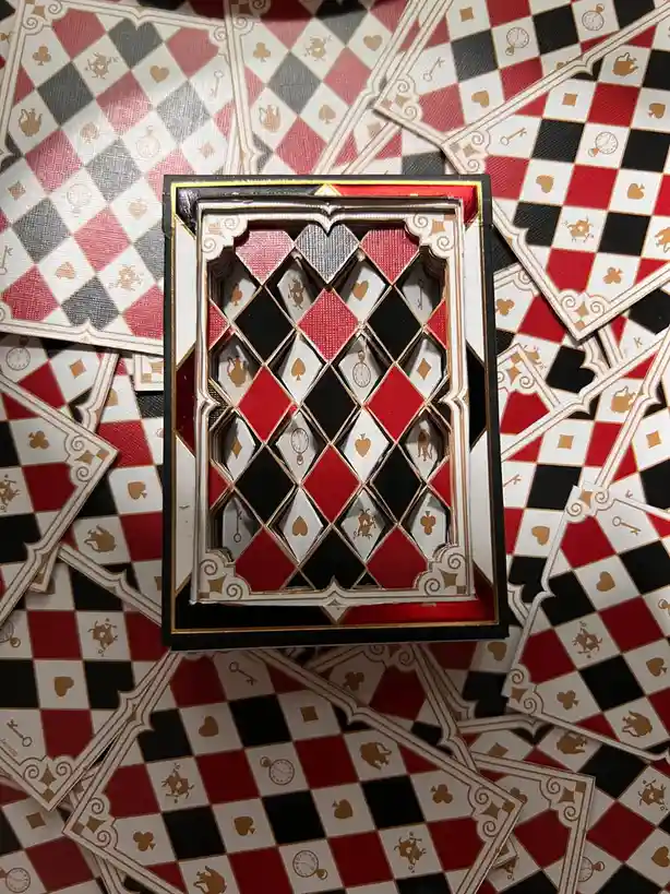 An ornate, decorative playing card box with a red, black, and gold diamond pattern is centered on a bed of identical…