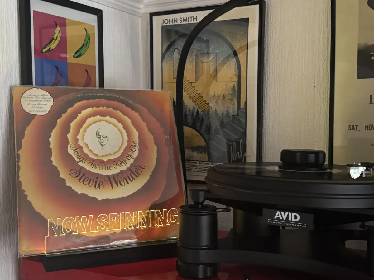 A vinyl record album titled 'Songs In The Key of Life' by Stevie Wonder is propped up next to a black AVID Sequel turntable…