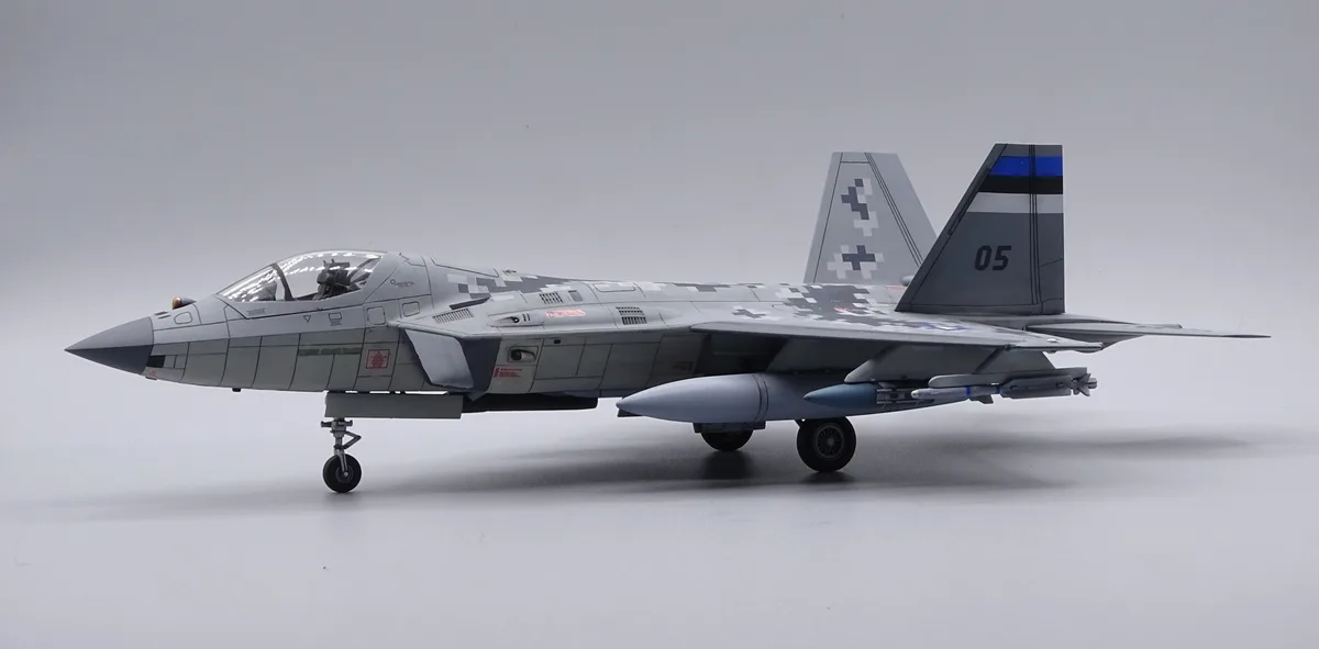 A detailed scale model of a fighter jet, likely an F-35, is shown in profile against a plain gray background. The aircraft…