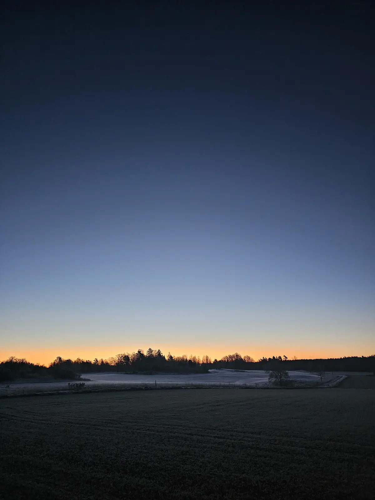 A serene landscape photo of a frost-covered field at dawn or dusk, with a gradient sky transitioning from deep blue to…